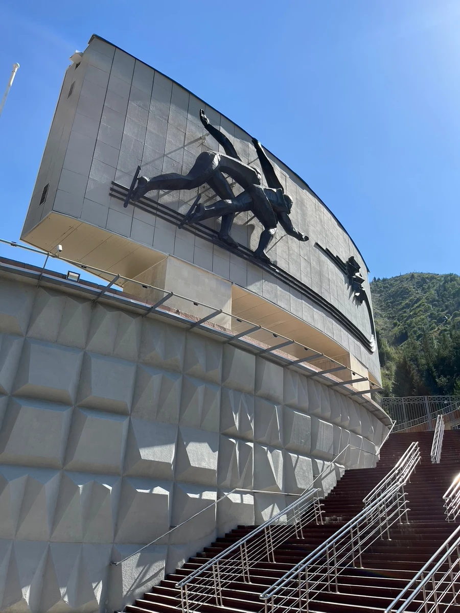 Long stairway leading up to the Medeu skating rink building with a large speed-skater relief sculpture on its facade